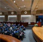 Samhita Rhodes, professor of engineering, speaks on stage in academic regalia to an audience at faculty convocation in Loosemore Auditorium